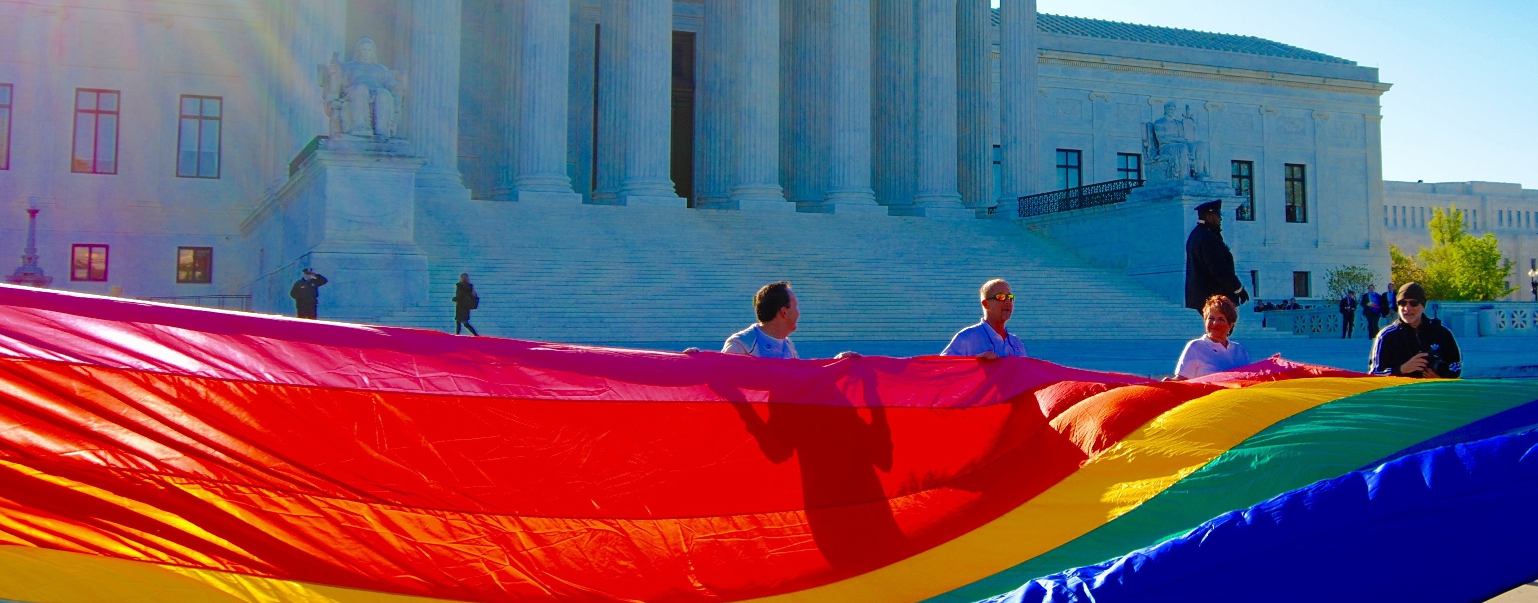 Several people hold a large pride flag in front of the Supreme Court