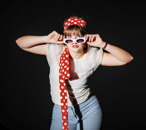 A student model poses in sunglasses and a red and white polka dot headband
